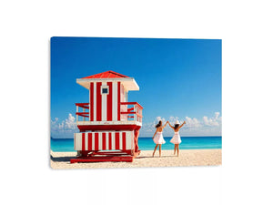 Minimal coastal beach scene with red lifeguard hut blue ocean and two women walking aesthetic Canvas Print