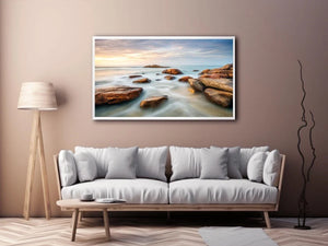 Serene coastal landscape wall art featuring smooth ocean waves, natural shoreline rocks, pastel sunrise sky, and luxury long exposure beach photography for modern coastal interiors