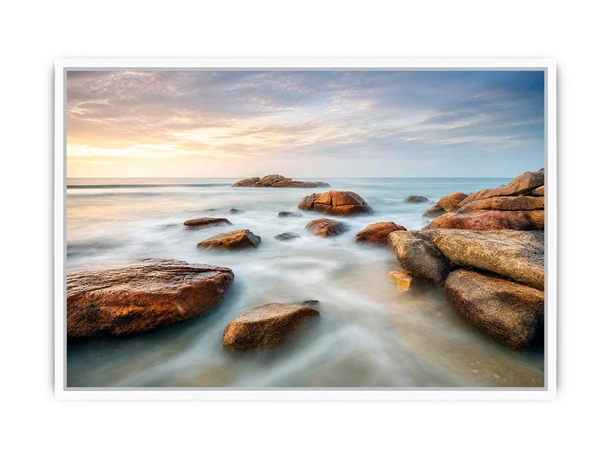 Serene coastal landscape wall art featuring smooth ocean waves, natural shoreline rocks, pastel sunrise sky, and luxury long exposure beach photography for modern coastal interiors